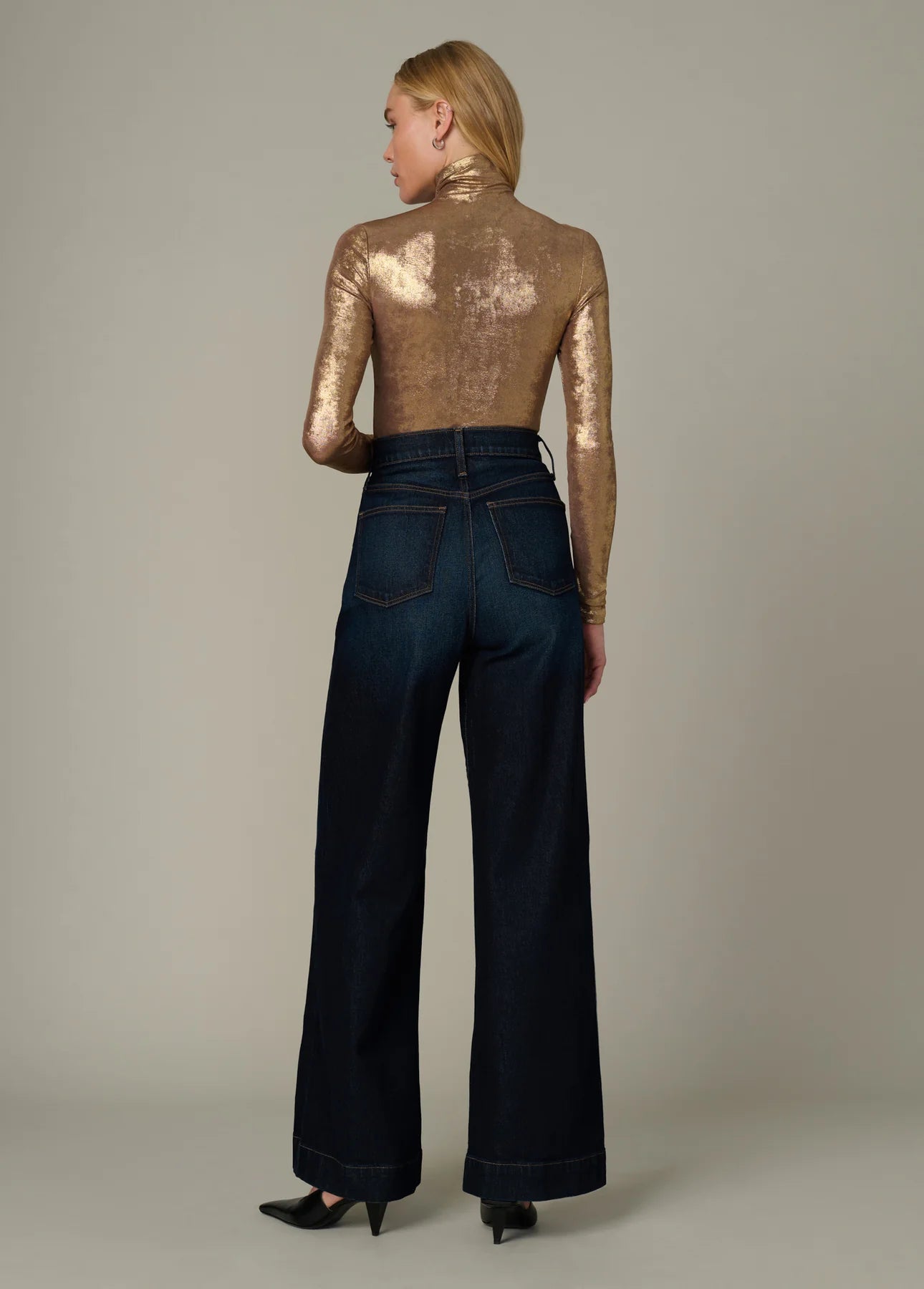Model wearing the Tony Top in metallic gold with a funnel neckline and long fitted sleeves paired with dark wide-leg jeans.