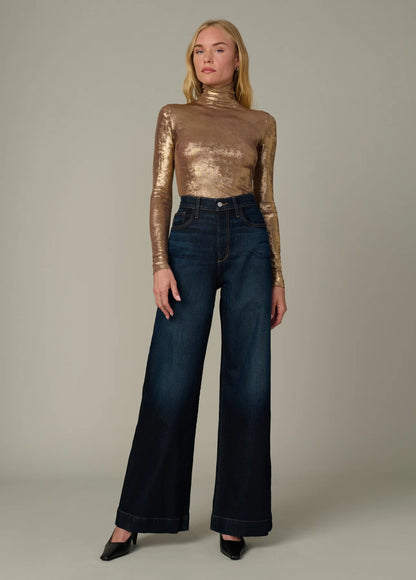 Full-body front view of the Tony Top in metallic gold featuring a fitted silhouette, funnel neckline, and long sleeves styled with dark wide-leg denim.
