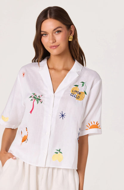 Model wearing the Vesa Embroidered Linen Button-Up Top in white with colorful summer motif embroidery, short sleeves, and a relaxed cropped fit.