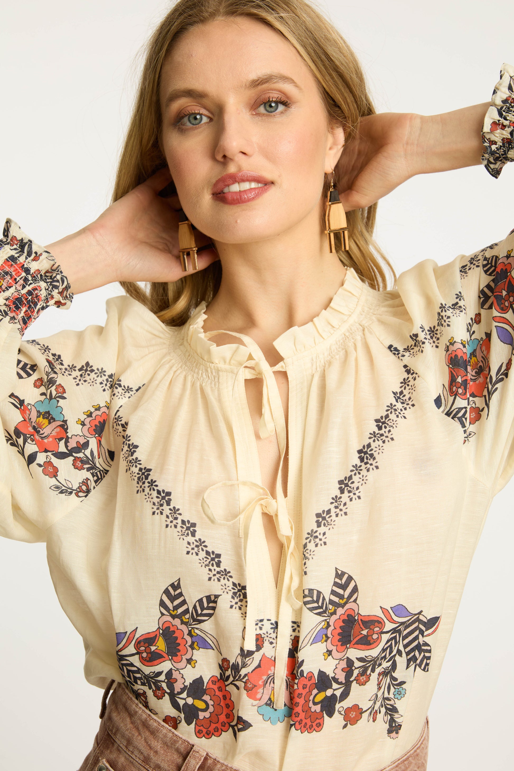 Close-up of the Vickie Top in Zebra Leaf featuring floral embroidery, ruffle-trim neckline, tassel tie details, and soft cream fabric with voluminous sleeves.