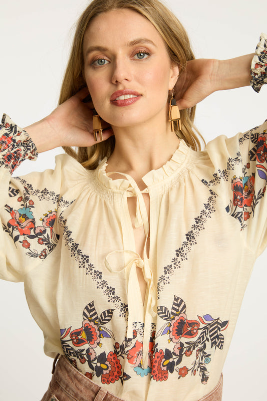 Close-up of the Vickie Top in Zebra Leaf featuring floral embroidery, ruffle-trim neckline, tassel tie details, and soft cream fabric with voluminous sleeves.