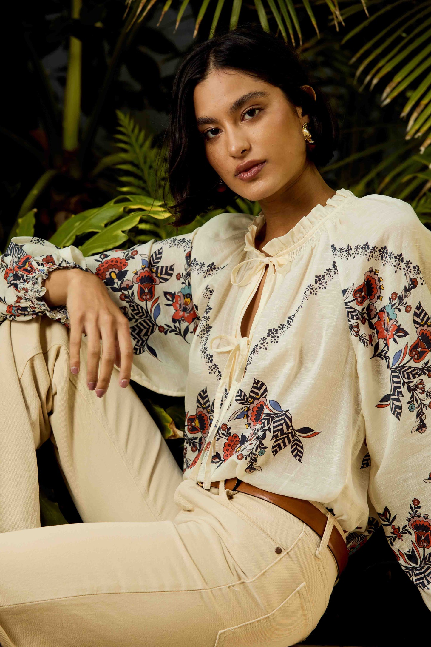 Model wearing the Vickie Top in Zebra Leaf styled with cream trousers in a tropical resort setting, featuring embroidered floral details and a relaxed boho-inspired fit.