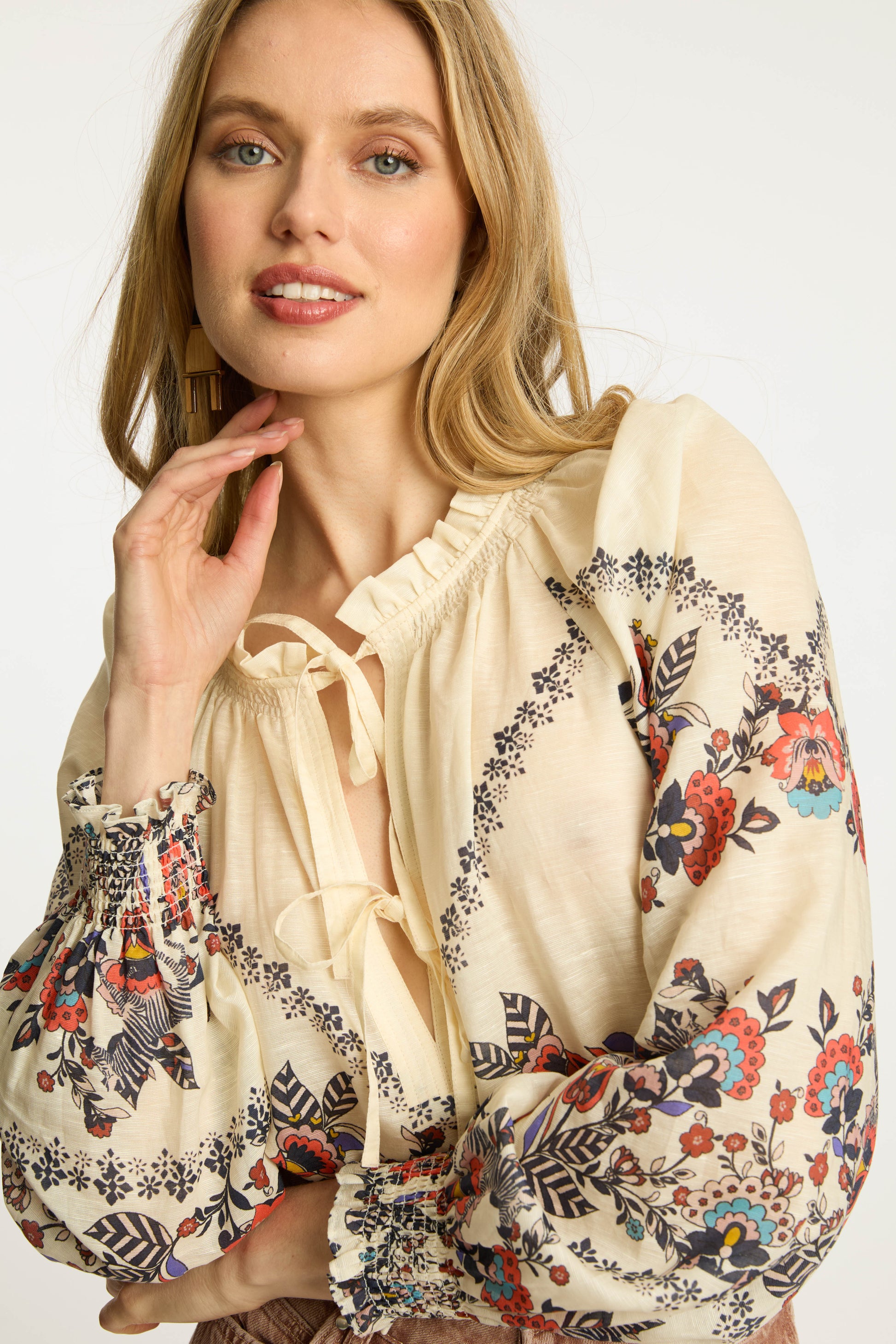 Portrait view of the Vickie Top in Zebra Leaf highlighting the embroidered floral print, smocked ruffle cuffs, tassel tie neckline, and relaxed bohemian silhouette.