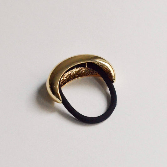 Gold-toned wide crescent metal ponytail hair tie with a black elastic, shown at an angle.