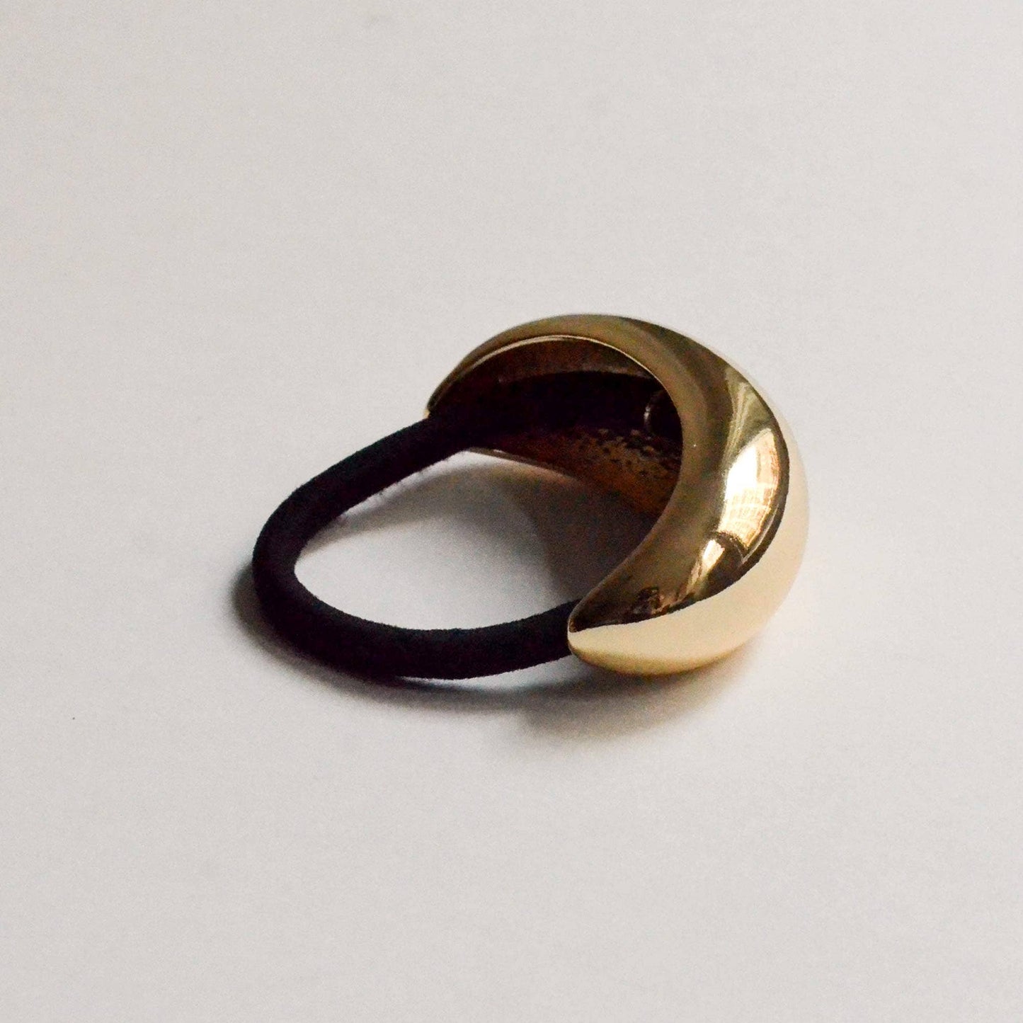Side view of a polished gold crescent metal ponytail hair tie with a black elastic.