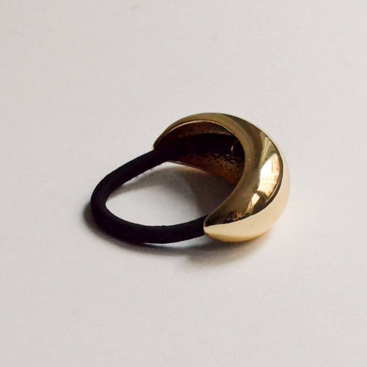 Side view of a polished gold crescent metal ponytail hair tie with a black elastic.
