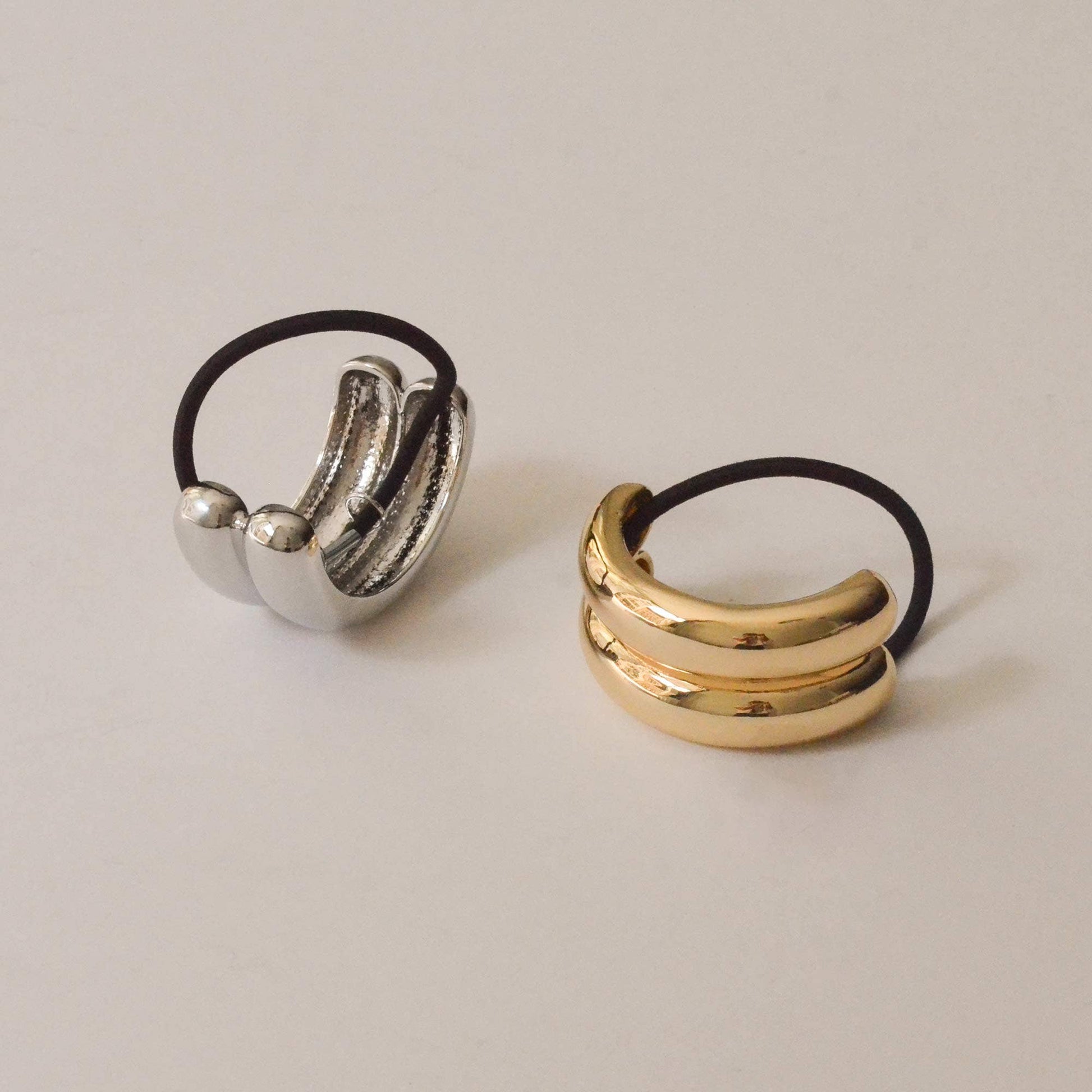 Gold and silver wide double arch metal ponytail hair ties displayed together with black elastics.