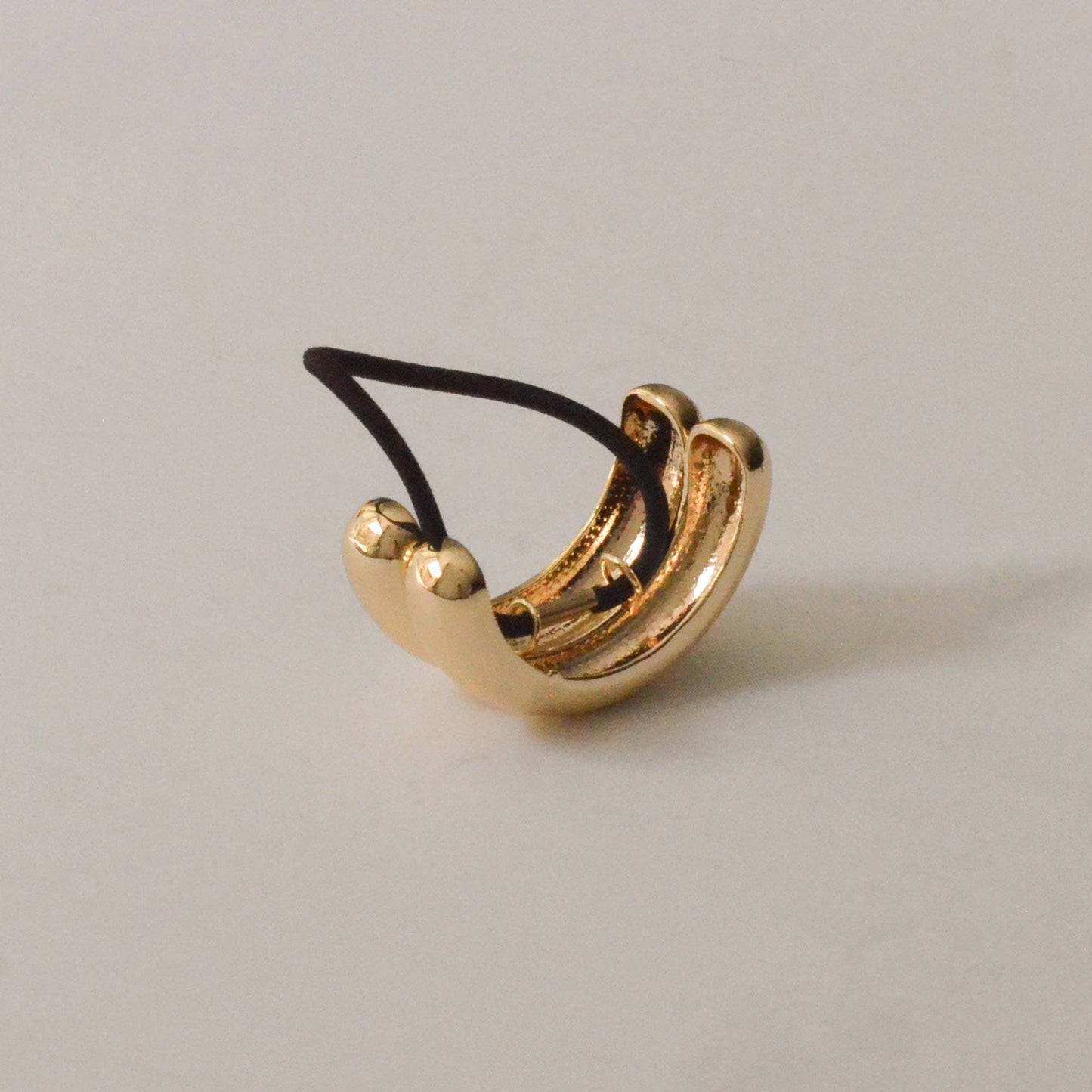 Angled view of the sculptural gold double arch ponytail hair tie and black elastic.