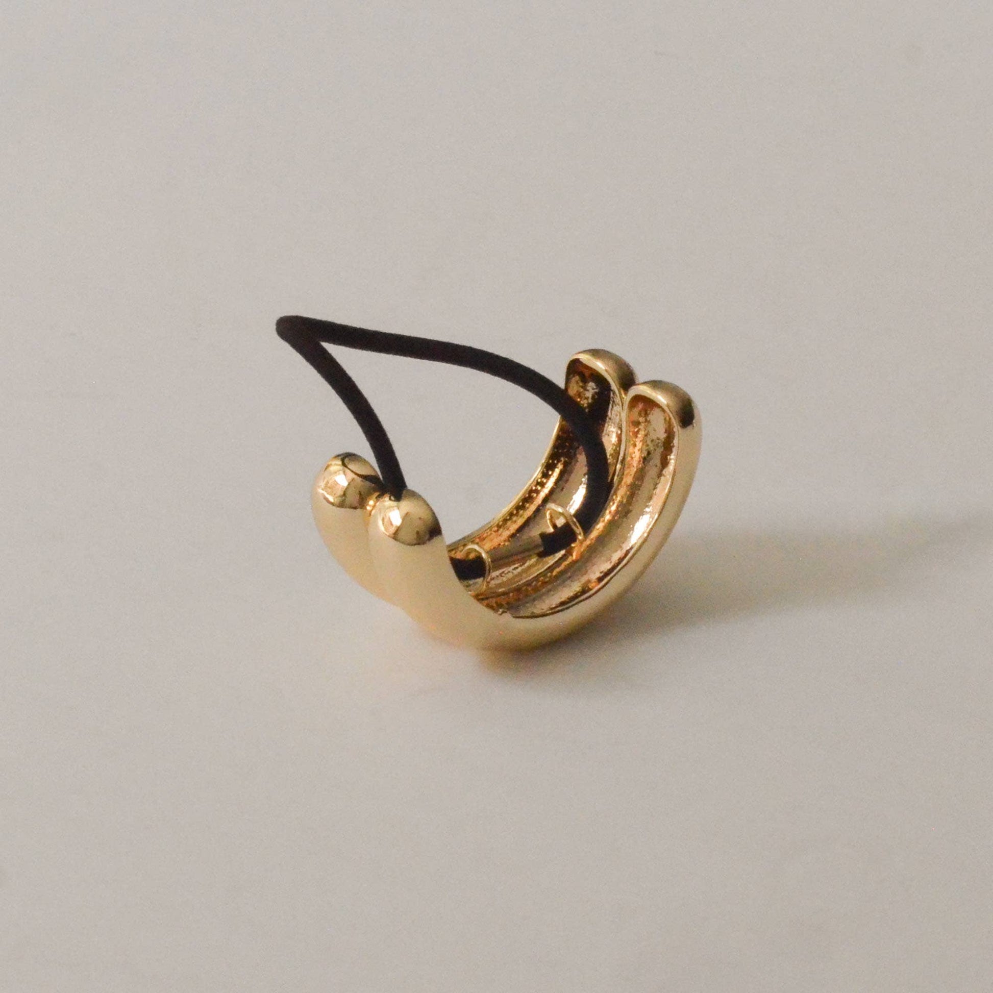 Angled view of the sculptural gold double arch ponytail hair tie and black elastic.