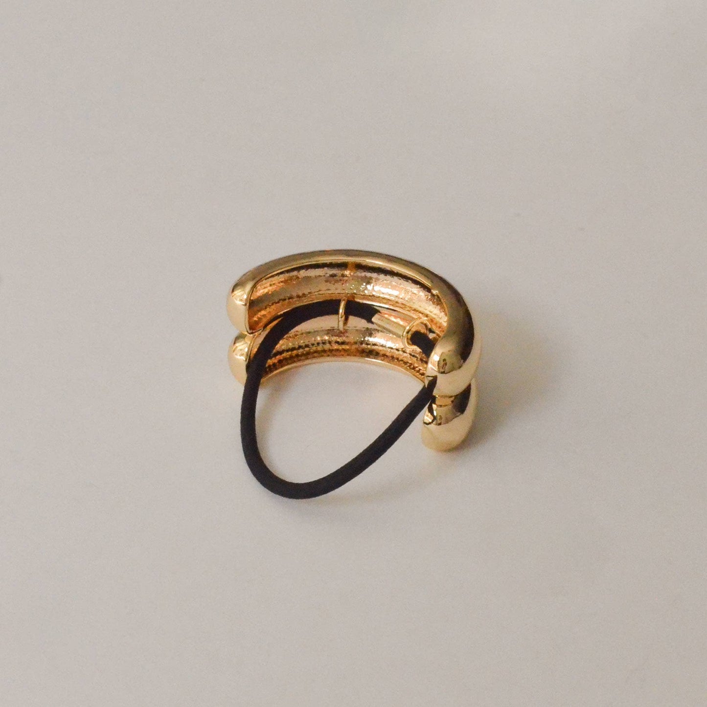 Back view of the gold double arch metal ponytail cuff with attached black elastic.