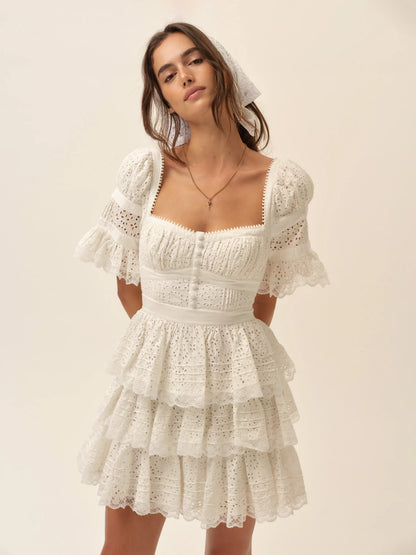 Model wearing the Willa Mini Dress in white featuring a square neckline, puff sleeves, corset-inspired bodice, and tiered ruffle mini skirt.