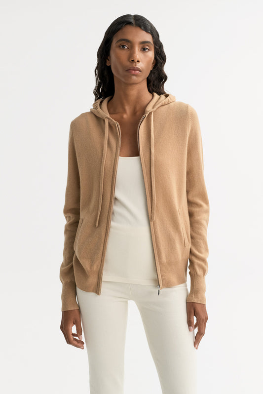 Model wearing a camel cashmere zip hoodie layered over a cream top with front pockets and ribbed trims
