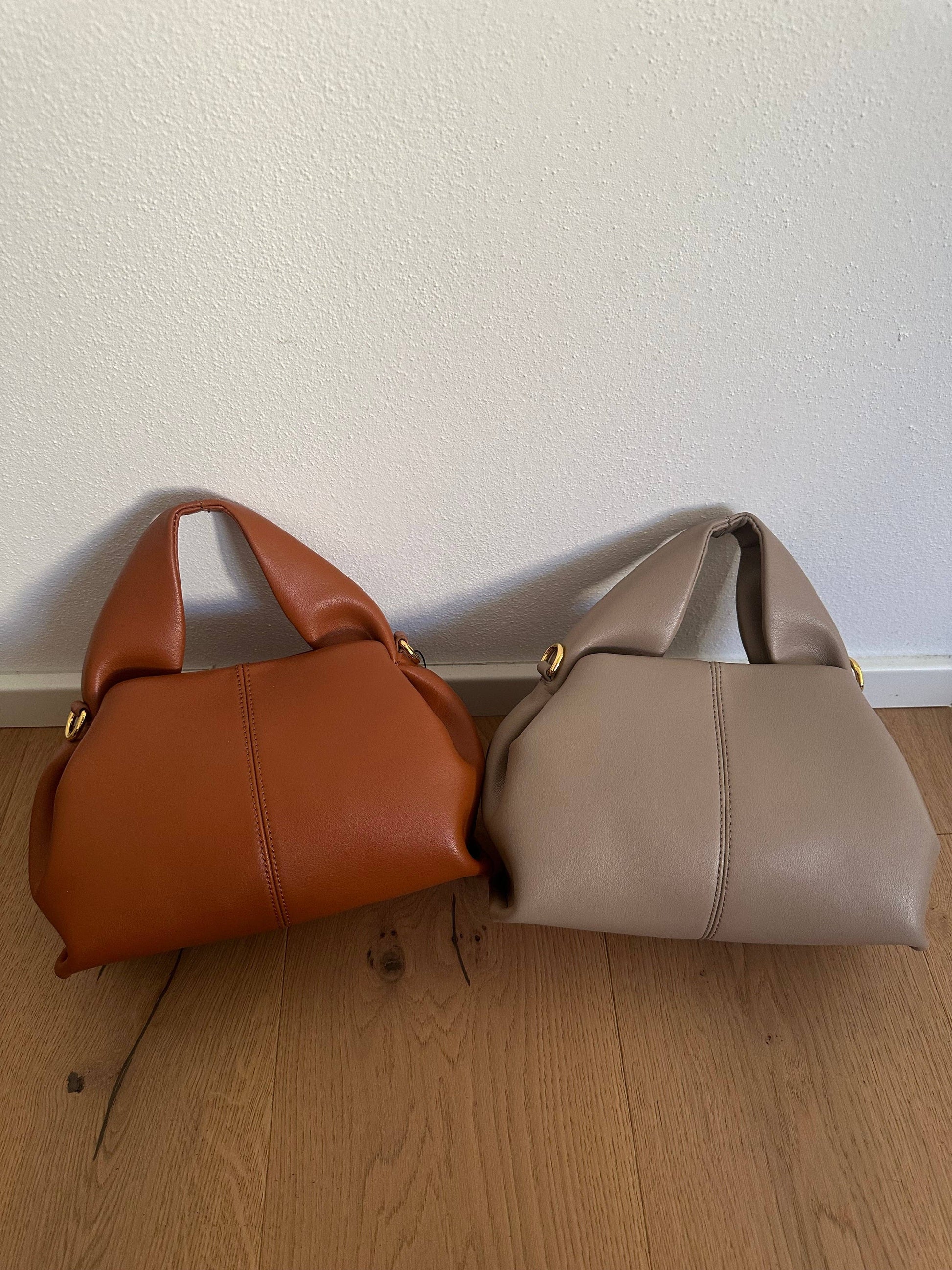 Two Zoe Premium genuine calf leather bags in cognac brown and taupe, shown side by side with padded top handles and gold-tone hardware.
