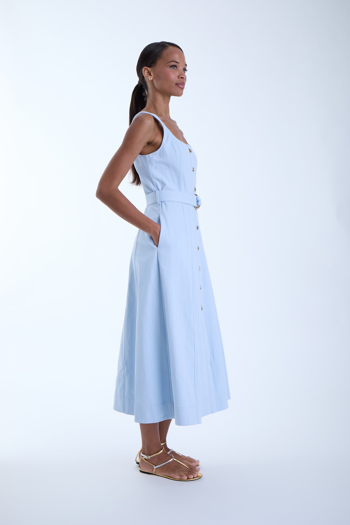 Side view of the Zyra Denim Midi Dress in sky blue showing the sleeveless shape, belted waist, side pockets, and flared midi-length silhouette.