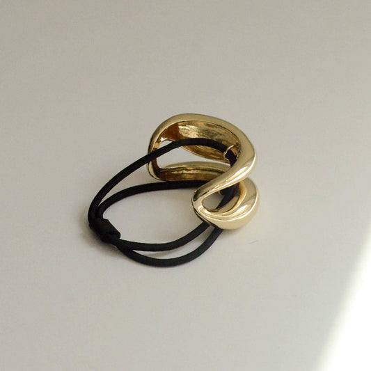 Gold sculptured metal hair tie shown upright from an angled view